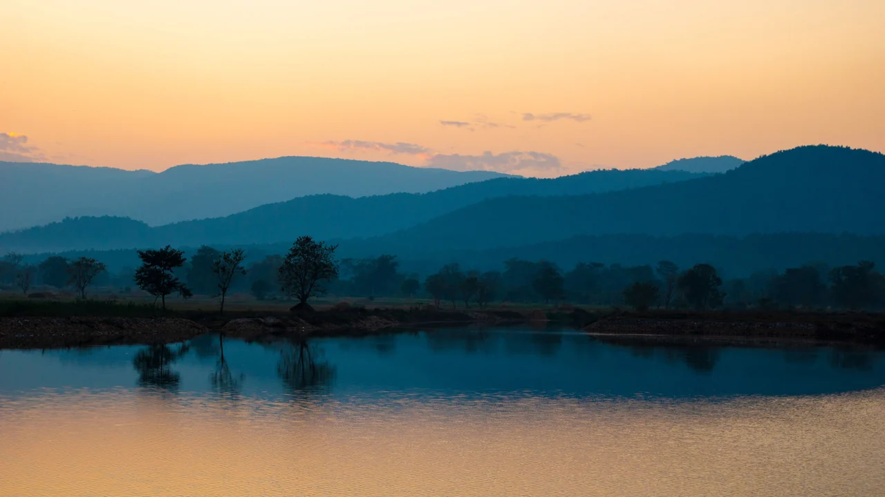 Teal mountains reflected in a still lake at golden hour